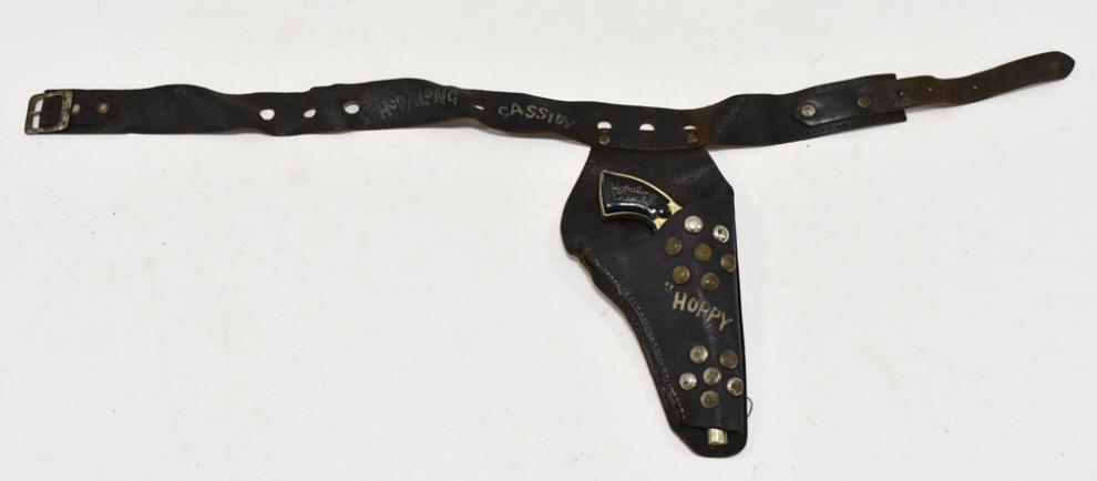 Gold Wyandotte Hopalong Cassidy Cap Gun w/ Holster: Gold Wyandotte Hopalong Cassidy cap gun with Hopalong Cassidy leather holster. The cap gun has some wear from use and age. The holster has some cracking and wear from age. The gun measures approximate