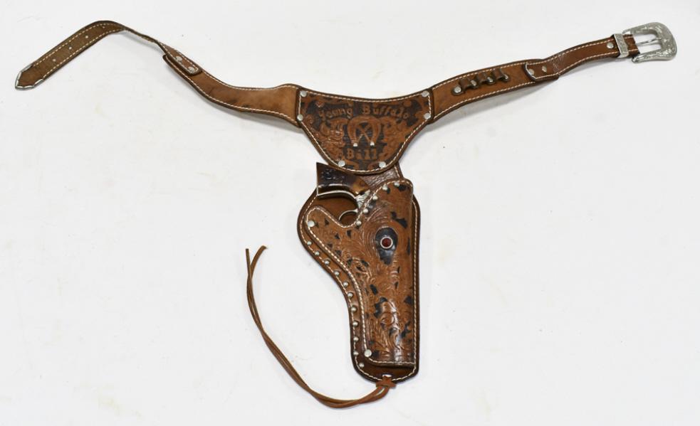 Young Buffalo Bill Cap Gun w/ Leather Holster: Young Buffalo Bill cap gun with matching Young Buffalo Bill leather holster. The cap gun has some corrosion and wear from use and age. The holster has some cracking and wear from age. The gun measures