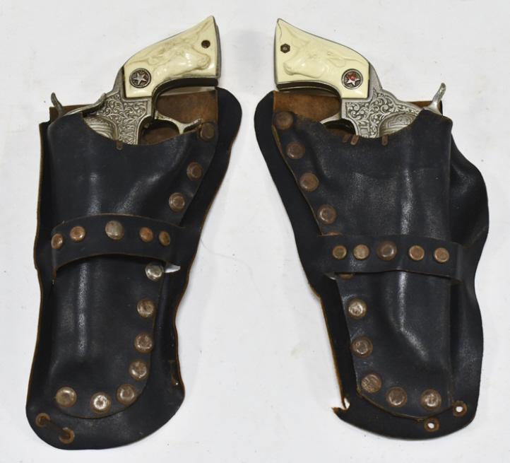 Hubley Texan Cap Gun Set w/ Holster: Hubley cast iron Texan cap gun set with leather holster. The holsters are missing the belt. Some of the grips are cracked. The guns have corrosion and wear from use and age. The holster has some crack