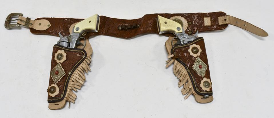 Nichols Stallion 38 Cap Gun Set w/ Leather Holster: Nichols Stallion 38 cap gun set with leather holster. The cap guns have some corrosion and wear from use and age. The holster has some cracking and wear from age. Each gun measures approximately 9" lo