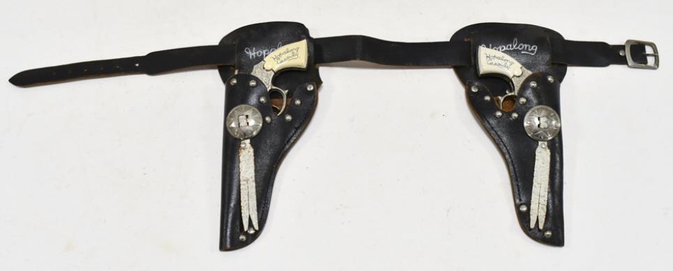 Wyandotte Hopalong Cassidy Cap Gun Set w/ Holster: Wyandotte Hopalong Cassidy cap gun set with Hopalong Cassidy leather holster. The cap guns have some corrosion and wear from use and age. The holster has some cracking. Each gun measures approximately