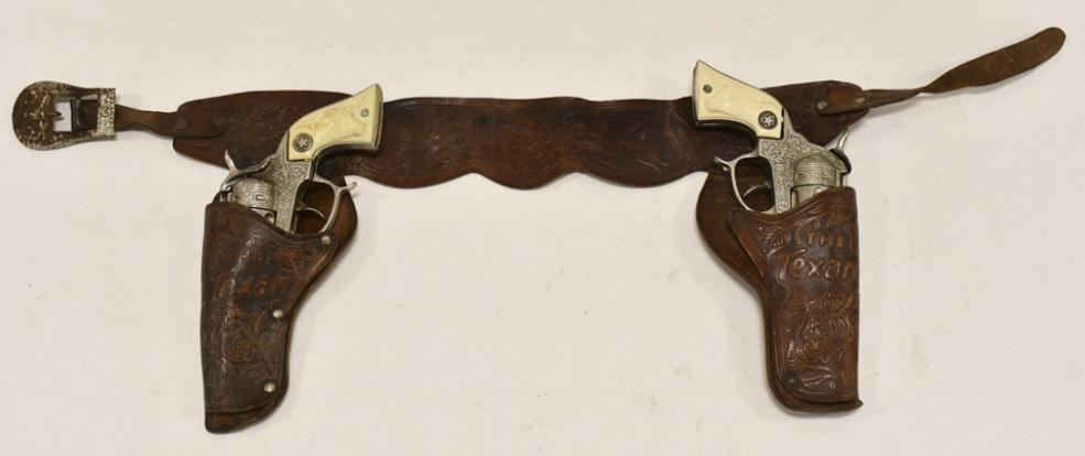 Hubley Texan Cap Gun Set w/ Leather Holster: Hubley Texan cap gun set with leather holster. The cap guns have some wear from use and age. The holster has some cracking from age. Each gun measures approximately 9" long.