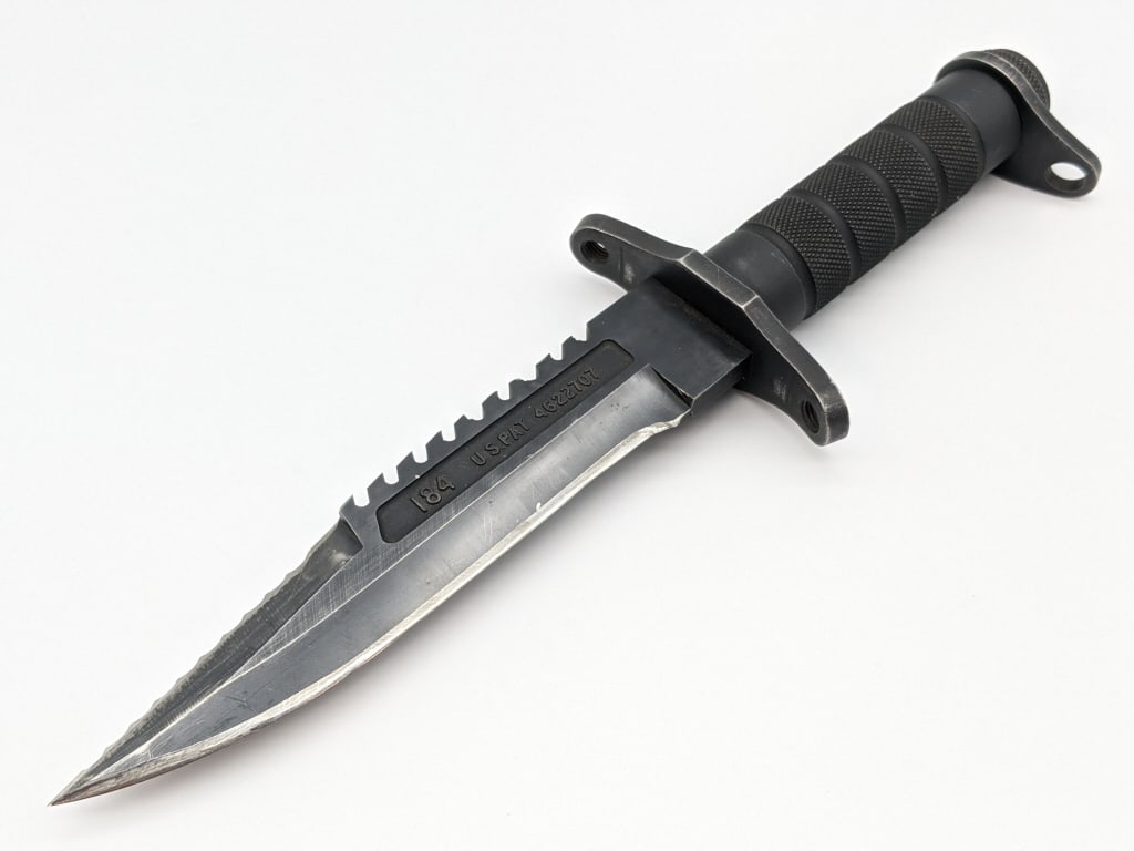 Buckmaster 184 Survival Knife: Buckmaster 184 Survival Knife. Knife features blade with two types of serrated spine, double guard, and stainless tube handle. Knife is in used condition with material loss from sharpening and wear fr