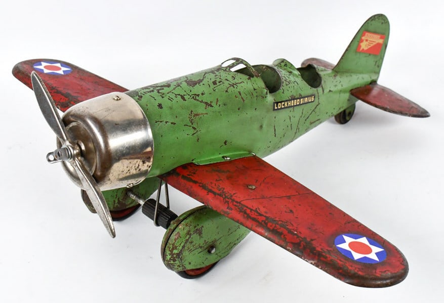 Original Steelcraft Lockhead Sirius AIrplane: Original Steelcraft Lockhead Sirus airplane. The decals are correct replacements. The plane has a green body with red wings. It has paint loss and wear from play and age. The wingspan measures approxi