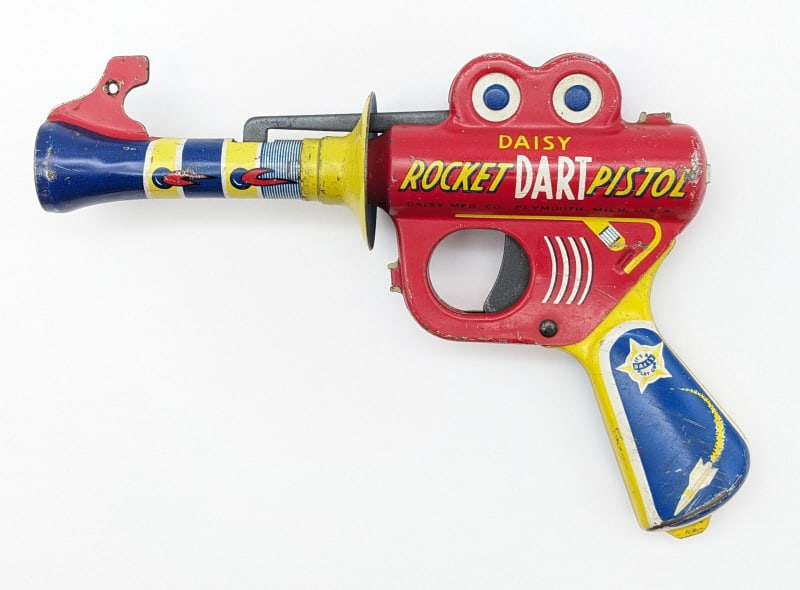 Daisy Tin Litho Rocket Dart Pistol Ray Gun: Daisy tin litho rocket dart pistol ray gun. The gun has scratches, paint loss, and wear from age / play. It is missing the dart. Displays well with good color and grpahics. Measures approximately 7-1/