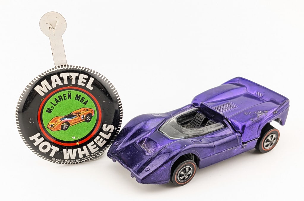 Hot Wheels Redline Magenta McLaren M6A - U.S.: Hot Wheels Redline magenta McLaren M6A with black interior and metal button. The car has some paint loss on the rear hood of the passenger side, but otherwise minor chips and toning to the rear hood.