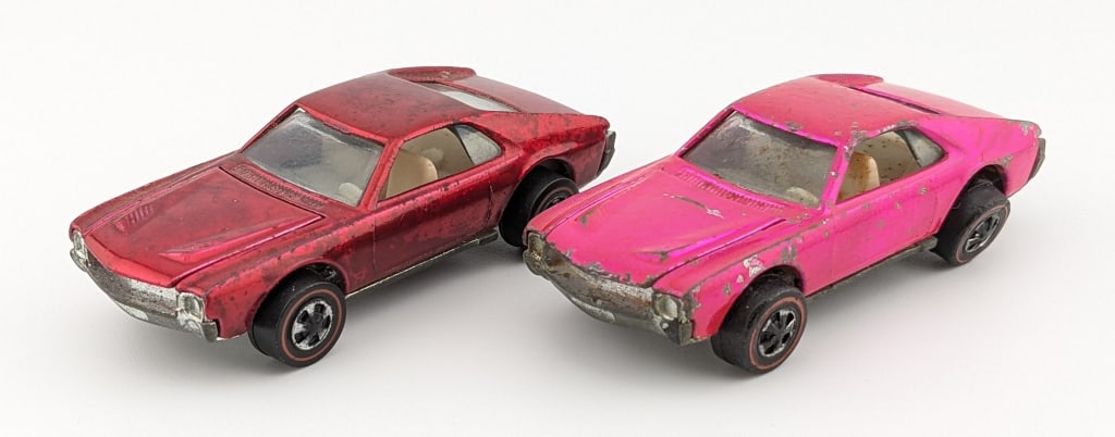 Hot Wheels Redline Rose & Hot Pink Custom AMX: Hot Wheels Redline rose and hot pink Custom AMX cars. The rose car has some toning to the roof and rear trunk area. The pink car has damage to the rear windshield, rubs, and paint loss.
