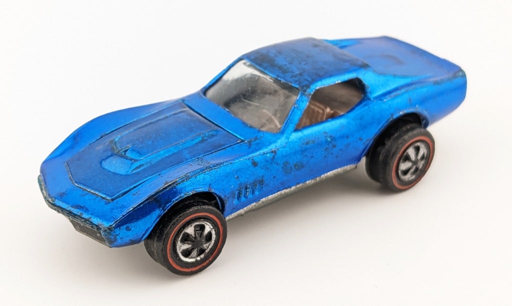 Hot Wheels Redline Blue Custom Corvette - U.S.: Hot Wheels Redline U.S. blue Custom Corvette. The corvette has some roof runs, dark spots on the rear trunk area, dullness to the base, and wear from age.