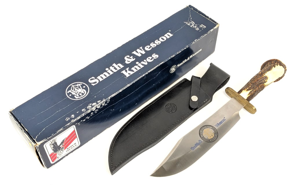 NIB 1998 Smith & Wesson Anniversary Bowie Knife: NIB 1998 Smith & Wesson Anniversary Bowie Knife w/ Sheath. Knife is numbered 278 and features a large clip point blade with etched branding, brass oblong double guard, and crown stag handle. Knife is