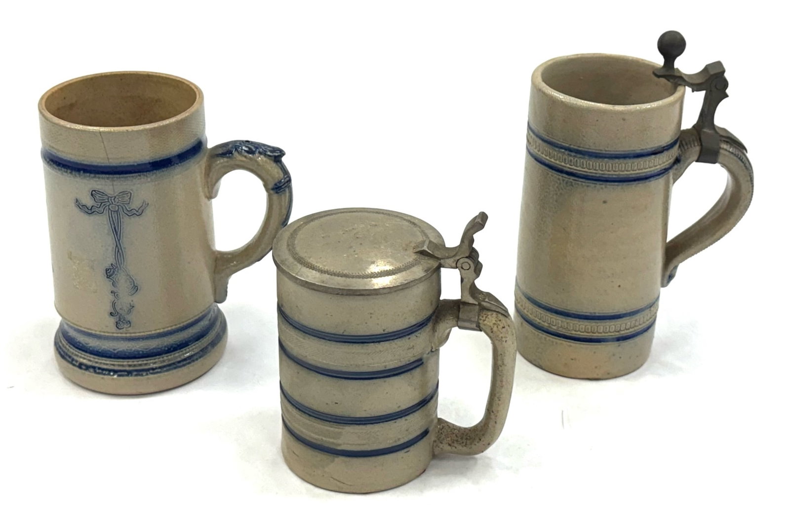 (3) Westerwald Cobalt Blue Salt Glaze Steins: (3) Westerwald Cobalt Blue Salt Glaze Steins. This Collection Of Steins Are Tan with Blue Striping. One Has A Complete and Functioning Flat Pewter Lid. The Sizes Range From 0.4-0.5 Liters.