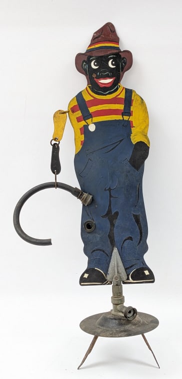 Vintage Black Sambo Yard Garden Sprinkler: Vintage Black Sambo Yard Garden Sprinkler. The double sided painted tin sprinkler is in good condition with age and use wear. The rubber hore has been cut. Overall measures approximately 35" tall x 8"