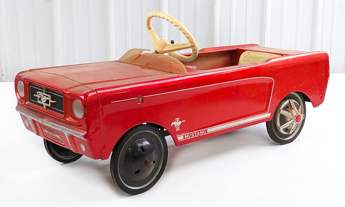 Original AMF Junior Ford Mustang Pedal Car: Original AMF Junior Ford Mustang pedal car. The car is missing two hubcaps, has a cracked windshield, cracked seat pad, discoloration, and wear from use / age. Measures approximately 39" long.