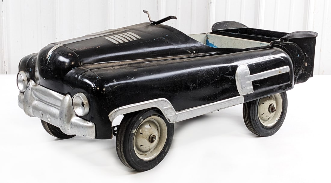 BMC Dump Truck Pedal Car: BMC dump truck pedal car. The car has an old repaint with pitting and age showing. It is missing the steering wheel. A good restoration or custom project candidate. Measures approximately 40" long.