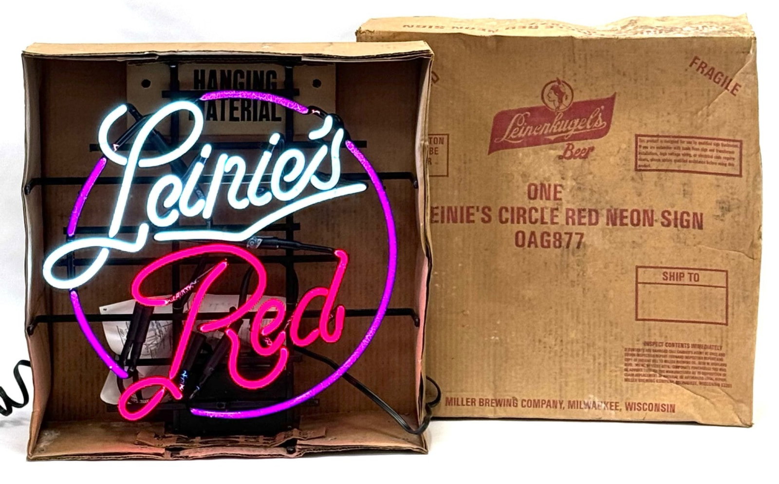 Leinenkugel's Leinie's Red Neon Advertisement Sign in Original Box: Leinenkugel's Leinie's Red Neon Advertisement Sign in Original Box. This Sign Is In Working Condition, This 3 Color Neon Sign Is Lit Up With The Outer Circle In Purple, The Word "Red" Lights Up In Red
