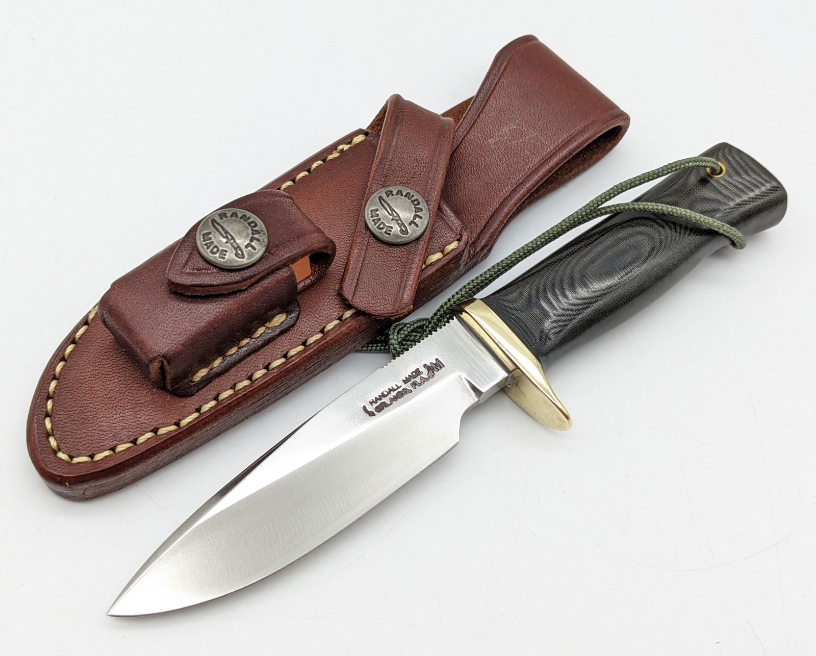 Randall Knife Society Model 28 Woodsman Miniature Knife w/ Sheath: Knife is in like new condition. Knife is numbered RKS 0037/261 and features thumb notches on the blade, a brass downturned single guard, and a black micarta handle with a lanyard hole. Comes with the