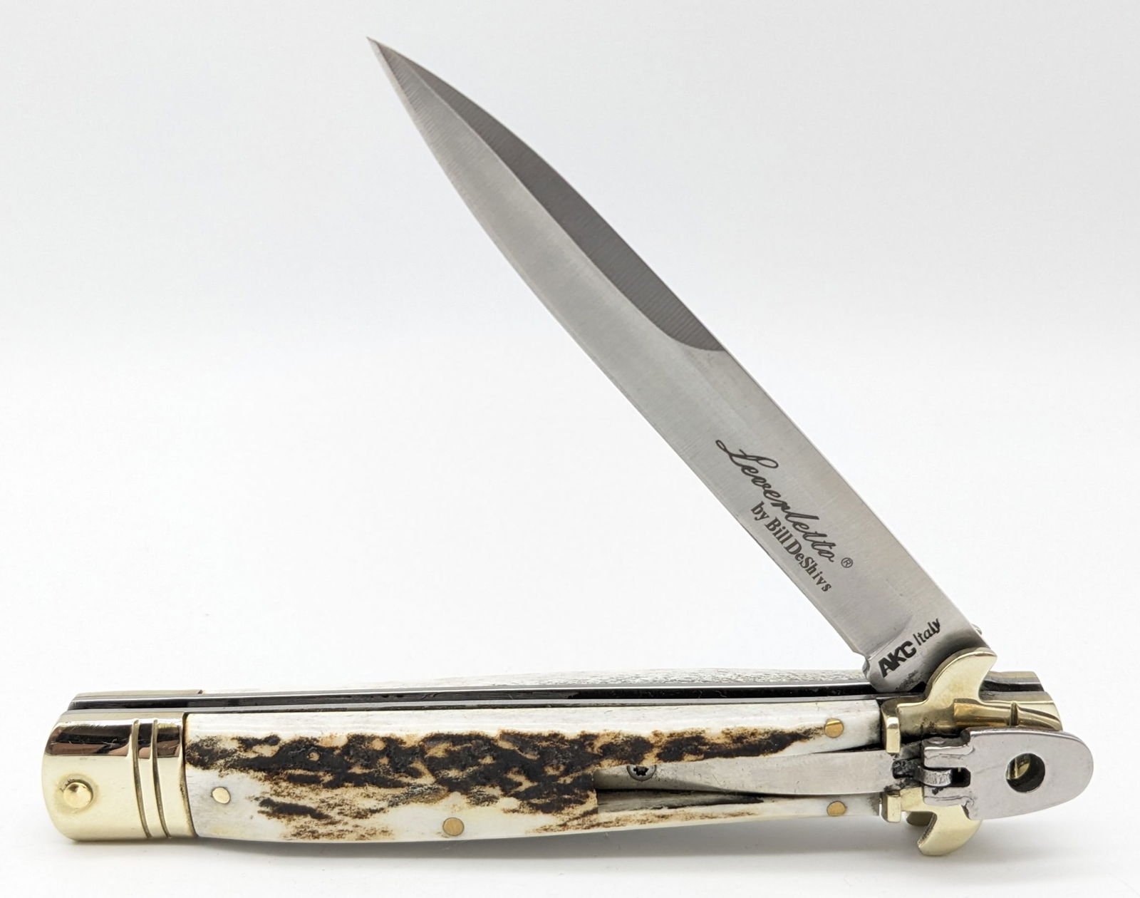 AKC Bill DeShivs Leverletto Stiletto Style Lever Lock Switchblade Knife: Knife features a stiletto style blade, serpentine brass bolster guard, and stag handle scales. Knife is in very nice condition with minimal wear from handling. Overall measures 5-1/2in when closed.