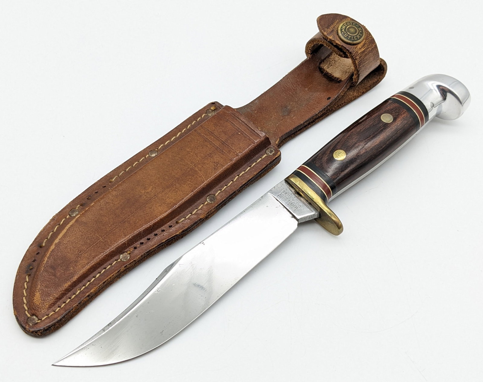 Western W36 Hunting Knife w/ Sheath: Knife features a mirror polished clip point blade, brass single guard, wood handle scales, and polished crows beak aluminum pommel. Knife is in nice aged condition with scattered carbon spotting and s