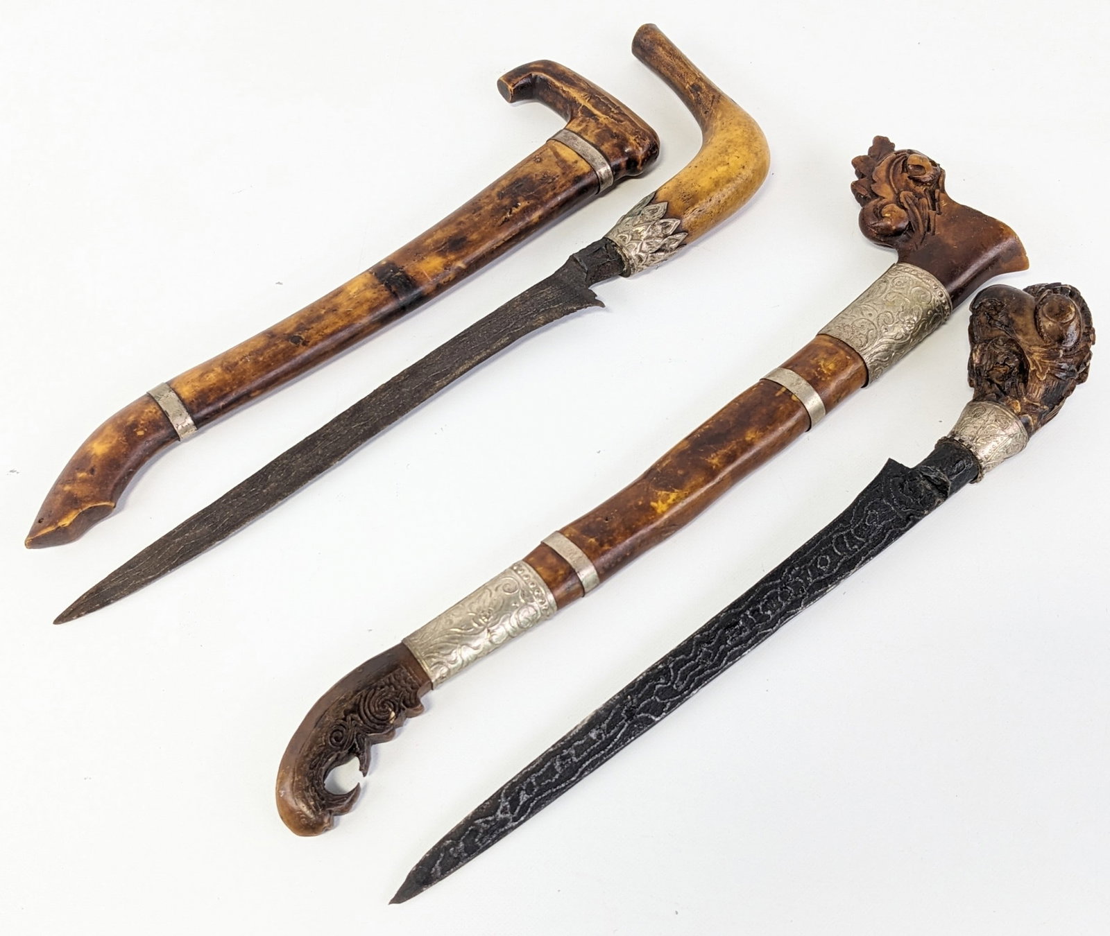 (2) Indonesian Badik Fixed Blade Knives w/ Sheaths: Knives feature folded steel blades with pronounced patters, and carved wood handles. The sheaths feature carvings and decorations similar to the style of the handle. Both knives are in nice aged condi