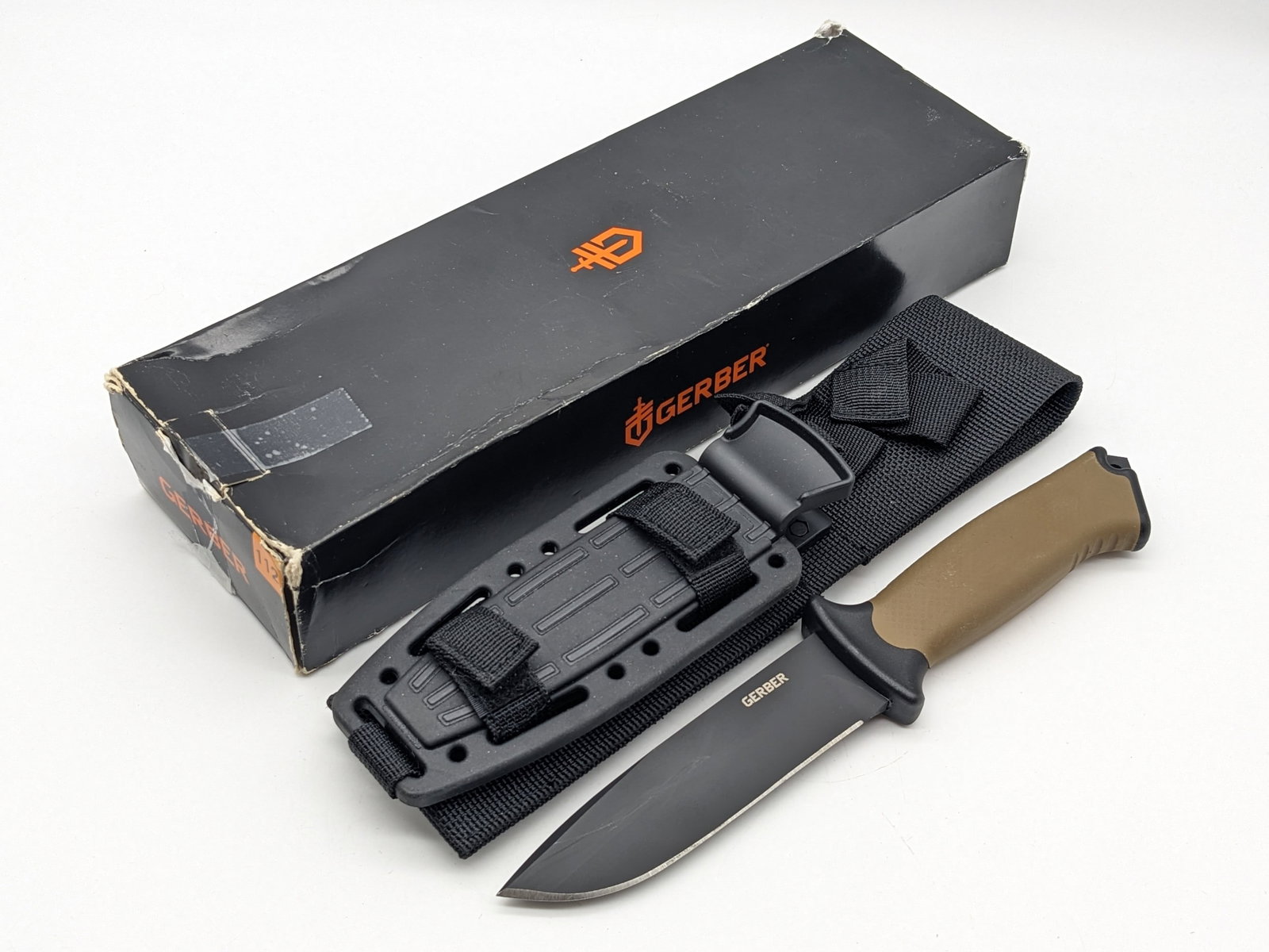 NIB Gerber Strongarm Fixed Blade Tactical Knife w/ Sheath: Features a black coated drop point blade, aluminum guard, coyote tan rubber handle, and crusher pommel with a lanyard hole. Knife is in new condition. Blade length measures 4-3/4in and overall 9-3/4in