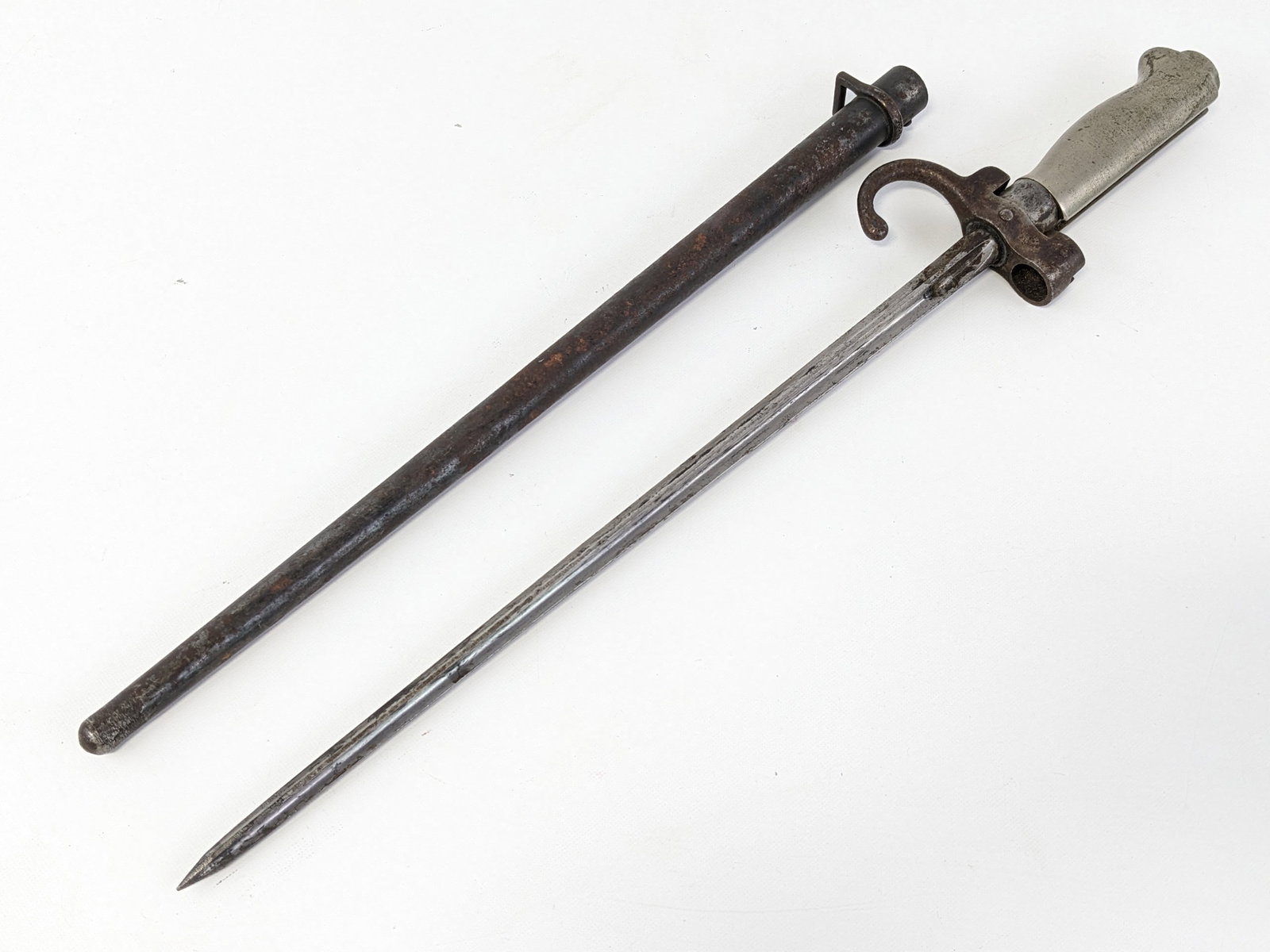 French M1886 Lebel Bayonet w/ Scabbard: Features an epee style blade with inspection marks, hooked quillon guard with inspection marks and serial number 54552, and steel handle. Bayonet is in fair aged condition with tarnishing and a few ru