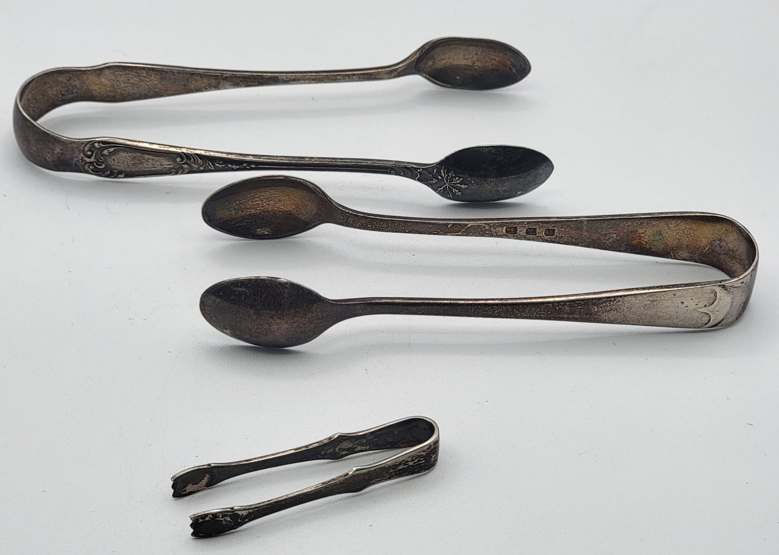 (5) Mixed Sterling Silver Flatware Pieces Including Tiffany: (5) Mixed Sterling Silver Flatware Pieces Including Tiffany. The lot includes two British Sterling sugar tongs, a teaspoon, a small ladle, and Tiffany & Co. saccharin tongs. The pieces are in nice con