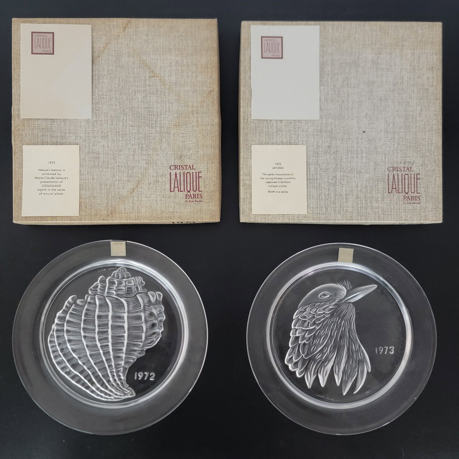 1972 & 1973 Lalique Crystal Annual Plates NIB: New In Box 1972 & 1973 Lalique Crystal Annual Plates. The 1972 is titled "Conch Shell" and the 1973 is titled "Bluejay". The plates are both signed and measure 8-1/4" in diameter. Designed by Marie Cl