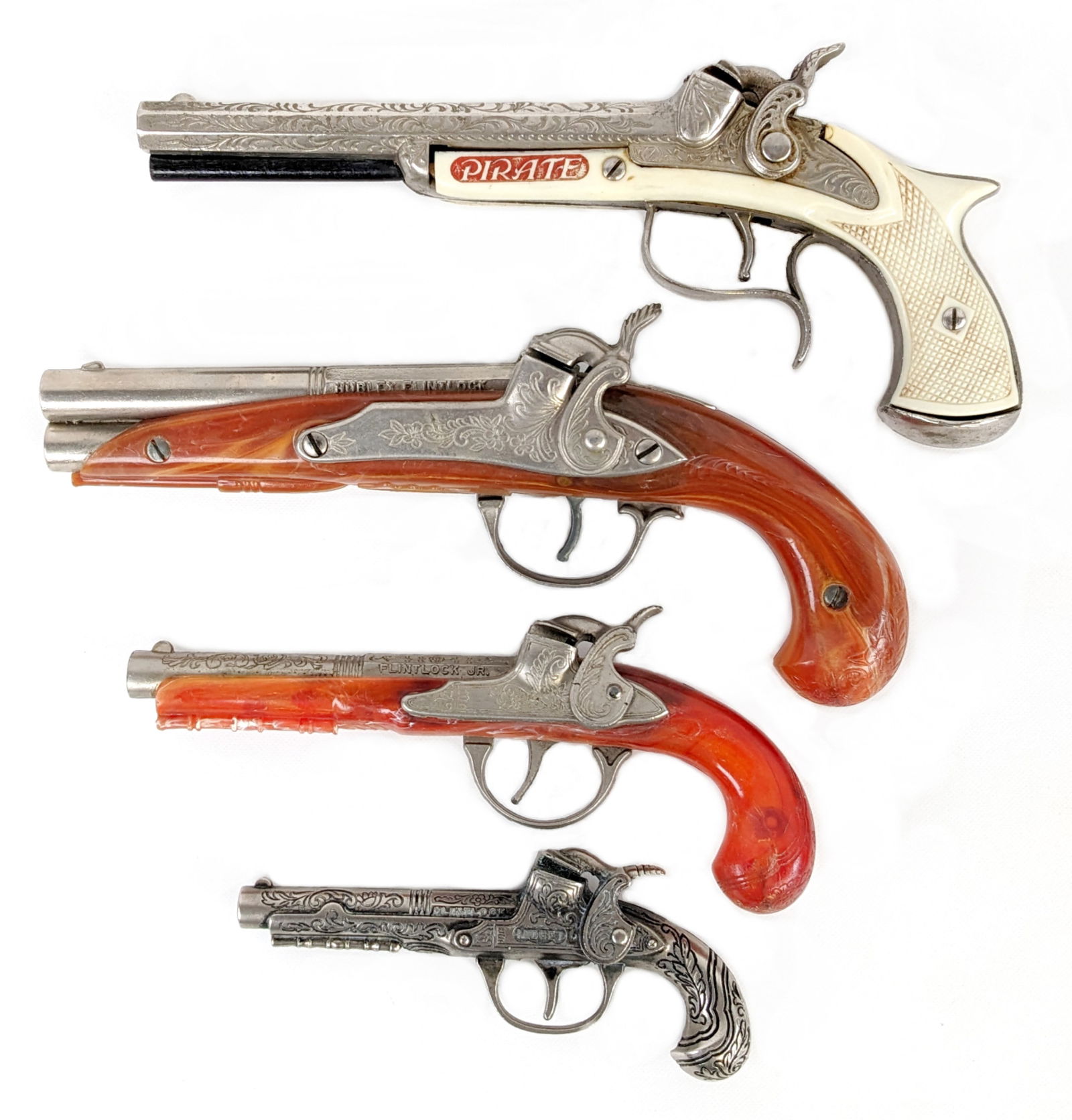 (4) Hubley Flintlock and Pirate Cap Guns: Includes Hubley Pirate flintlock cap gun, flintlock midget, flintlock jr., and Hubley flintlock cap gun pistols. All are in very good working condition. They may show some light use wear. Largest meas