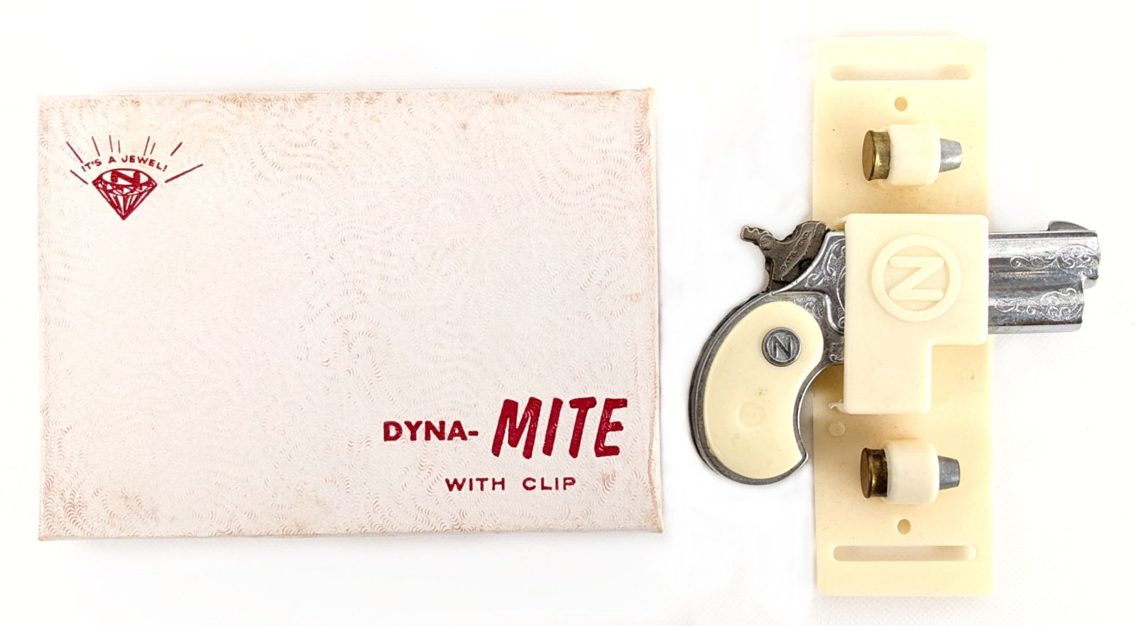 Nichols Dyna-Mite Cap Gun w/ Clip & Box: Nichols Dyna-Mite cap gun with clip and two cartridges in the original box. The gun is complete in the box. Appears to be in working order. The box shows light staining and wear from handling. Overall