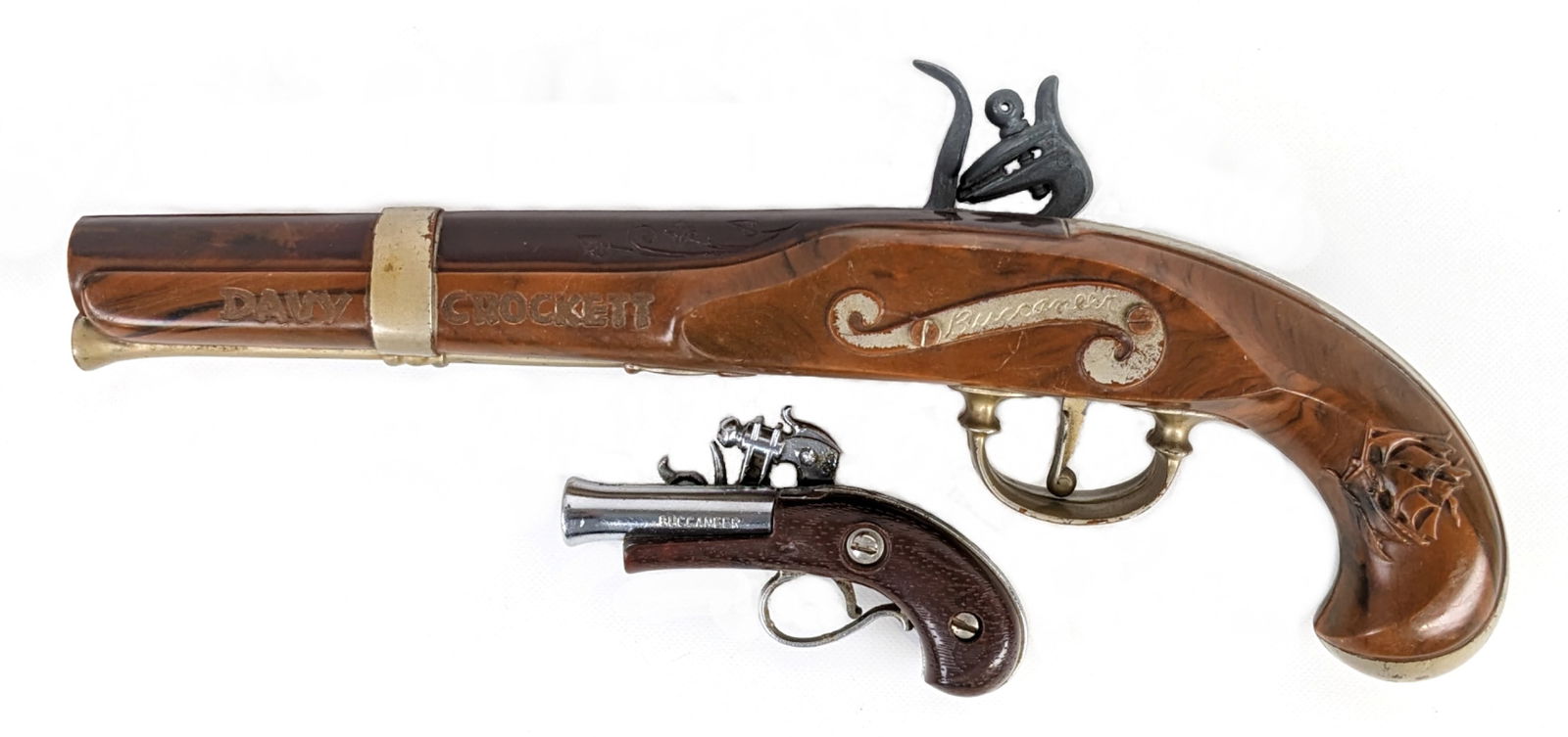 Davy Crockett Buccaneer & Nichols Buccaneer Flintlock Cap Guns: Davy Crocket Buccaneer flintlock cap gun and Nichols Buccaneer flintlock cap gun pistol. Both appear to function as they should. Both have some wear from use / age. Largest measures 10-1/2" long.