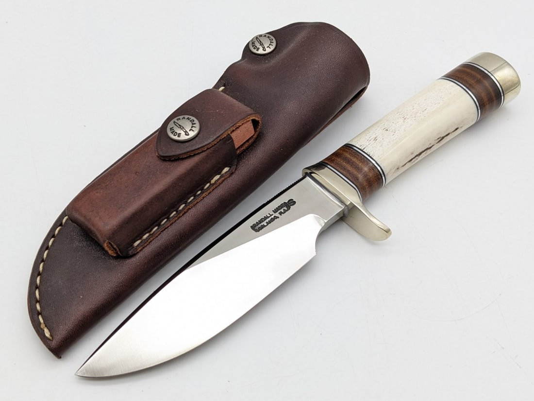 Randall Model 25 5in Smooth Bone Trapper w/ Sheath: Knife features a stainless steel blade with thumb notches, nickel downturned single guard, smooth wood handle with stacked leather spacers, and a nickel butt cap. Knife is in very nice condition with