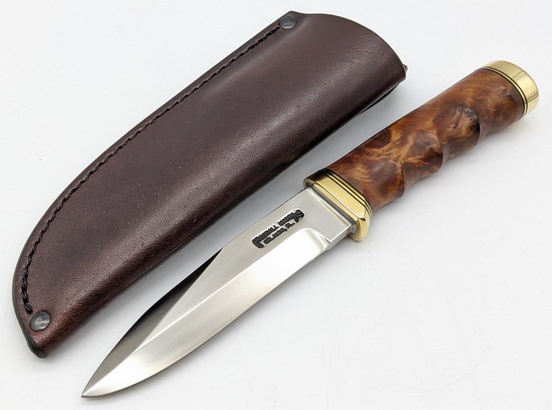 Randall 5in Finger Groove Thuya Burl Gambler: Knife features a stainless steel blade with thumb notches, brass reduced guard, finger groove thuya burl handle, and a brass butt cap. Knife comes with a Warlander Leather sheath and not the original.