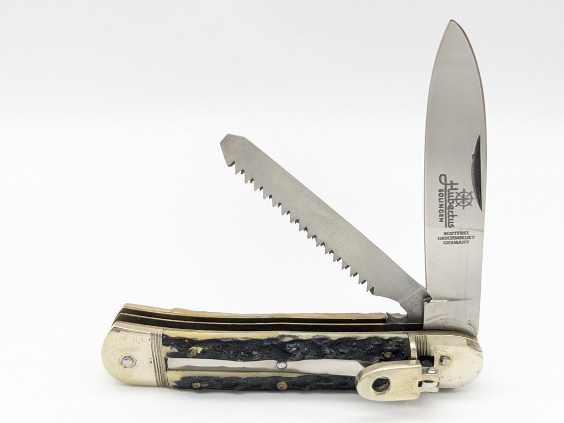 Hubertus Solingen Stag 2-Blade Leverlock Switchblade Knife: Features a secondary manual sawtooth blade. Knife is in very nice condition with tarnishing and light scuffs on the bolsters from handling and age. Overall measures 4-5/8in when closed.