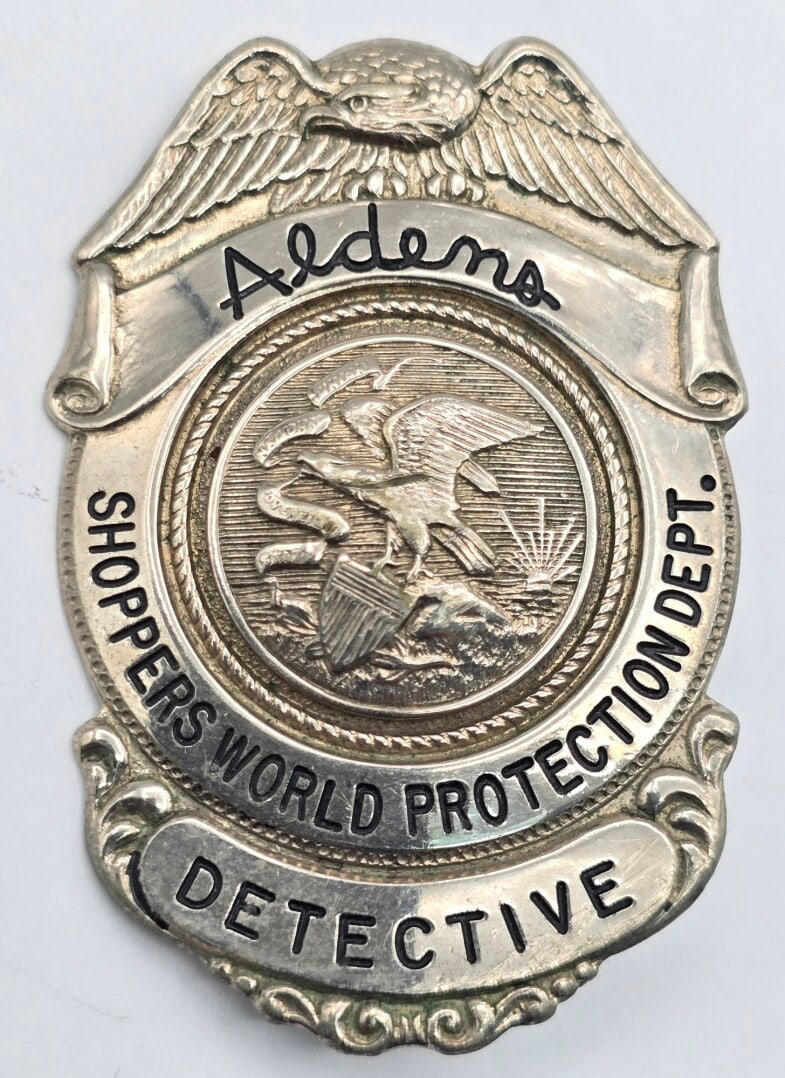 Obsolete Aldens Shoppers World Protection Department Detective Shield Badge: Obsolete Aldens Shoppers World Protections Department Detective Shield Badge. Badge is in nice condition with a pin back, has some light age and use wear. No maker mark. It measures approximately 2-1/