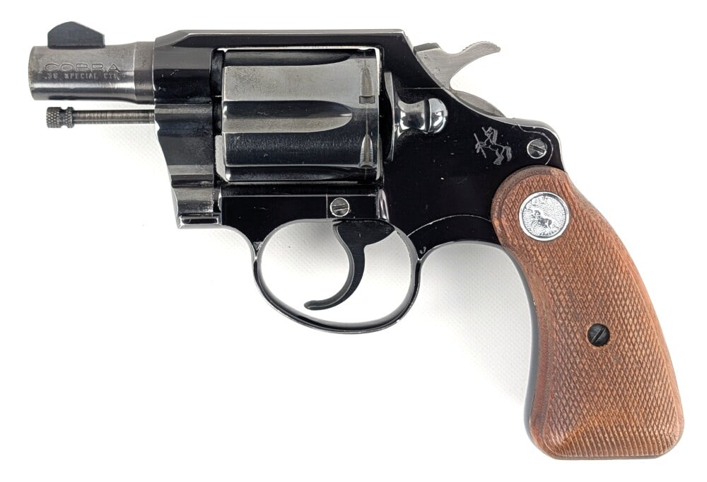 1963 Colt Cobra .38 Special Double Action Revolver: Manufacturer: Colt, Model: Cobra, Type: Revolver, Caliber/Gauge: .38 Spl, Barrel: 2 inch, Choke: , Finish: Blued, Grip: Checkered Wood, Stock: , Condition: Good with finish wear, and general scuffs an