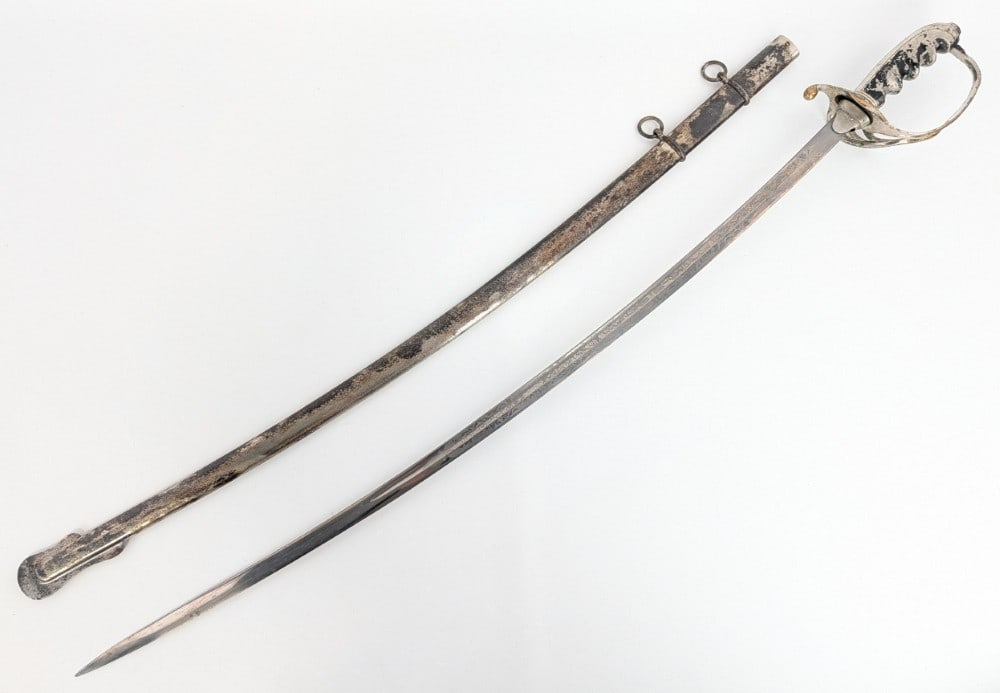 US M1902 Dress Sword w/ Scabbard: Features scroll and patriotic etching on the blade, a plated brass guard, and a plated brass finger groove handle. Sword is in fair condition with scratches and carbon spots on the blade, and scratche