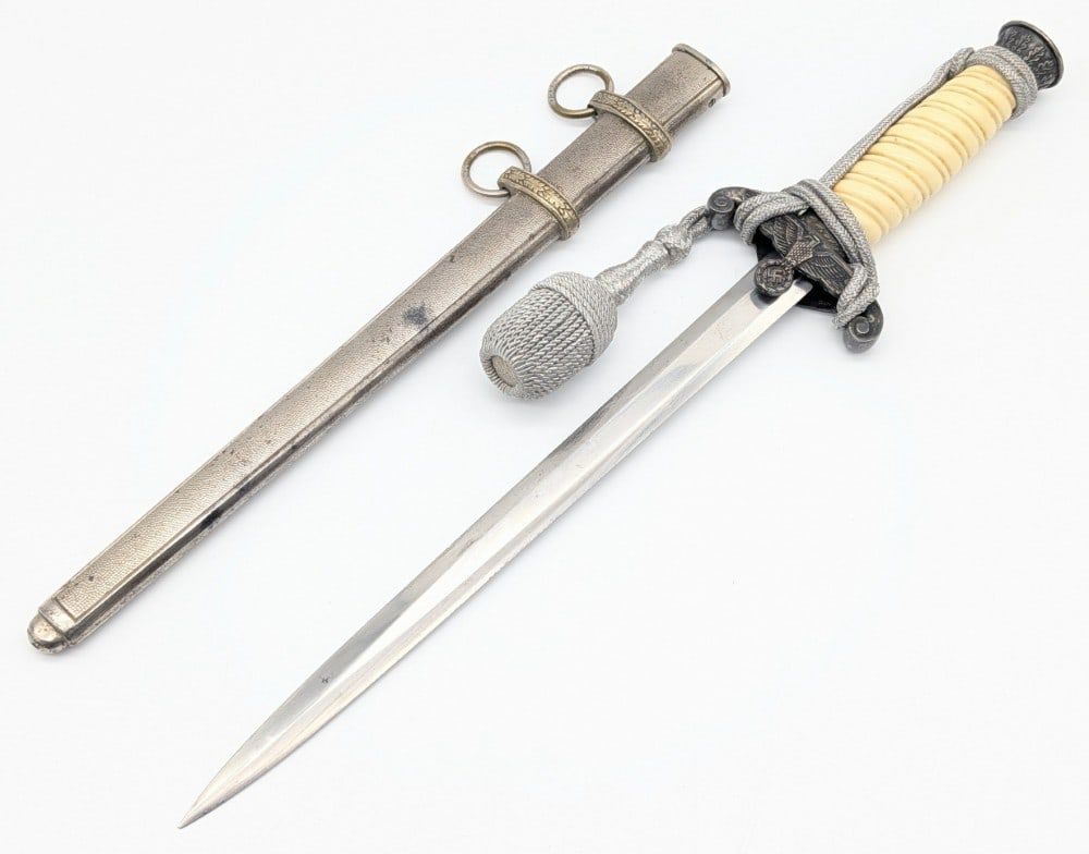 WWII German Unmarked Heer Dagger w/ Scabbard & Knot: Features a Nazi eagle guard, white plastic handle, and an oak leaf adorned pommel. Dagger is in good condition with some scratches and edge dings on the blade, scuffs on the handle, and general tarnis