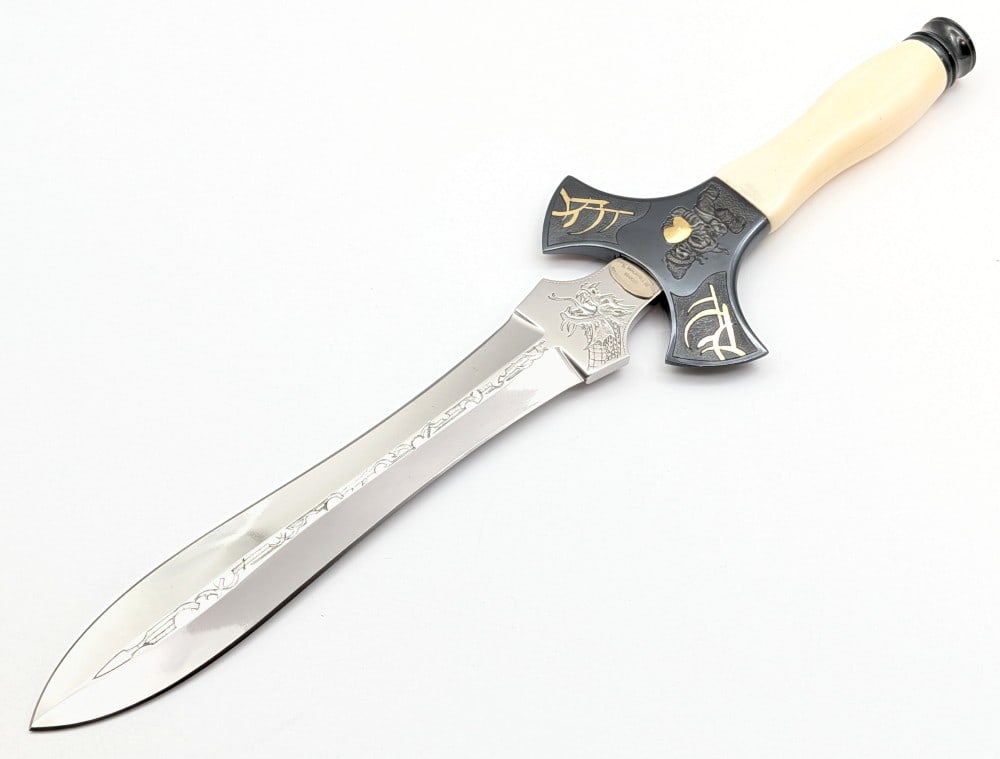 1998 Stephen Mackrill Fantasy Exotic Bone Double Edged Dagger: Features a mirror polished blade with mythical runes running down the center, a dragon on one side of the tang and a dragon bust on the other, an upswept blued finish flat double guard with fantasy en