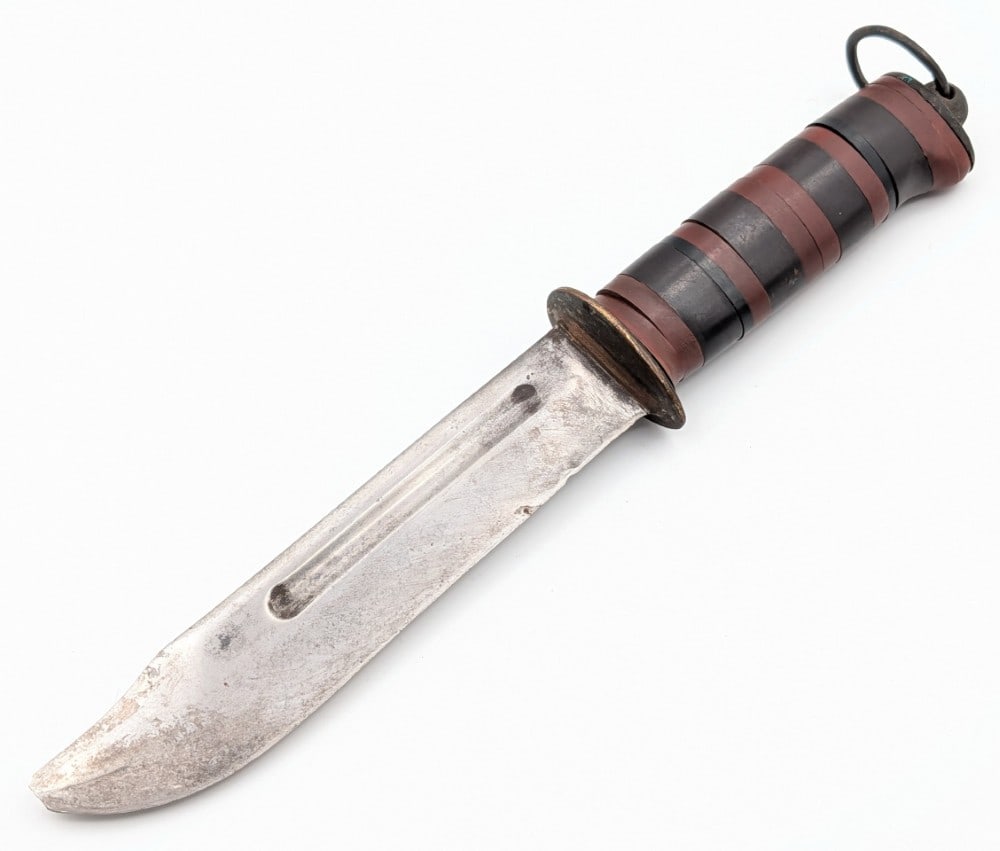 WWII Customized Pacific Theater Fighting Knife: Knife appears to use a Camillus or similar blade with a custom brass guard, stacked plastic handle, and original butt cap with a lanyard loop. Knife is in aged condition with heavy scratches and the t