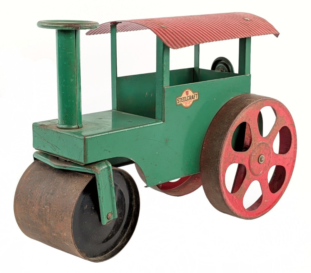 Original Steelcraft Ride On Steam Roller: Original Steelcraft ride on steam roller. The steam roller is green overall with a red roof, red rear wheels, and black roller. It has some paint loss and wear from play and age. Displays well with