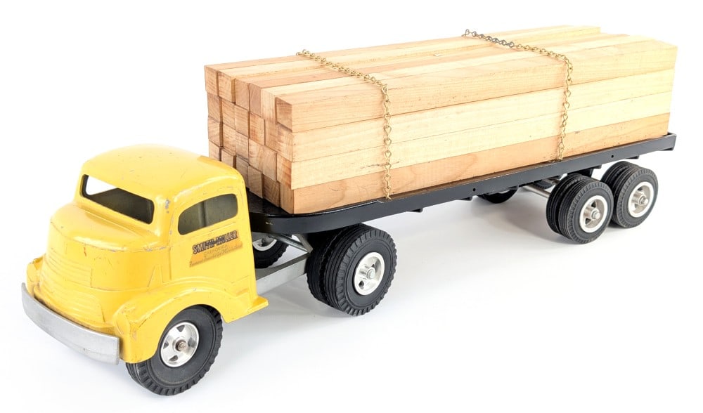 Smith Miller GMC Lumber Hauler Truck: Smith Miller GMC lumber hauler truck. The truck has paint chips on the cab. It has custom tires on the truck and a custom load of lumber. Measures approximately 23" long.