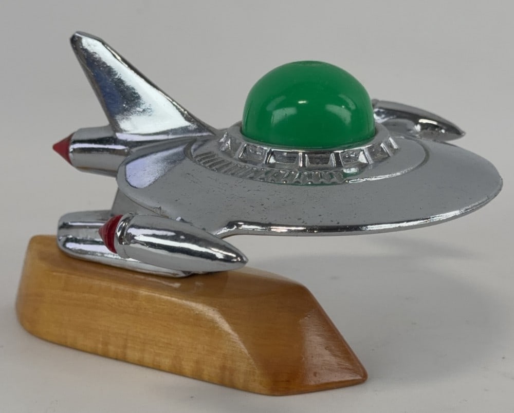 Alex Tremulis 1951 Spaceship Hood Ornament: Spaceship hood ornament with green plastic dome and all 3 red lights. Mounted to a wood base. Measures 7? long.