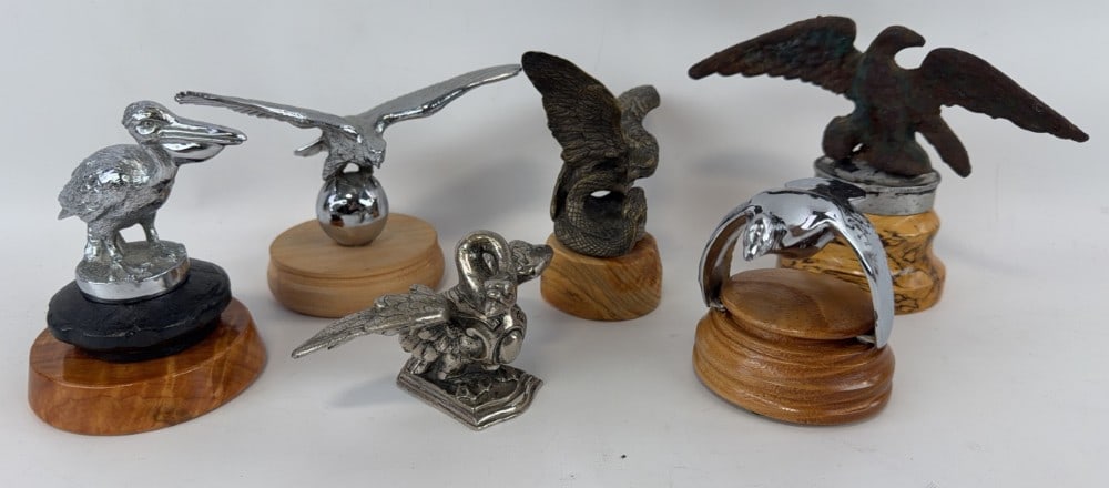 Lot of 6 Bird Hood Mascots: This lot includes a cast iron eagle mascot, chrome pelican, eagle on the world, eagle fighting a serpent, armored swan mascot and a Ford Model A flying quail ornament. Tallest is 5.75? with base.