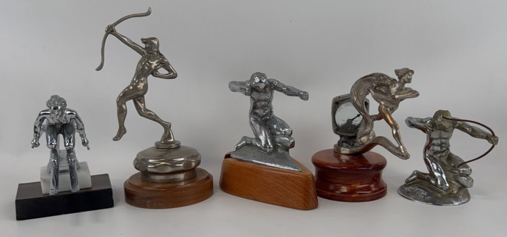 Lot of 5 Automobile Mascots: This lot includes 5 hood mascots including 3 Pierce Arrows (tallest marked Hofeller-Borden Co.), a down hill skier, and a Fleet of Foot mascot with Wilmot-Breeden calometer. Tallest 9?.