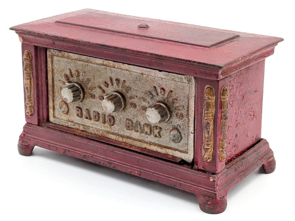 Kenton Cast Iron Radio Still bank: Kenton cast iron radio still bank. Painted in red overall with gold accents and unpainted door. The bank shows paint crazing and wear from use and age. Measures approximately 6" across by 3" deep by 3