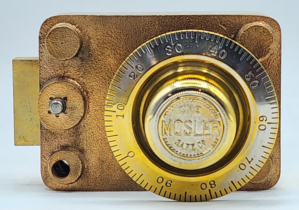 The Mosler Safe Co Combination Safe Dial And Lock Mechanism: The dial is marked 0-99 and the mechanism is encased in polished cast metal. The lock uses a single bolt locking point system. Worn due to age and use. Measures approximately 5" X 4_" X 3_"