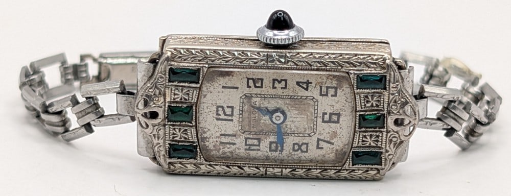 Ladies Art Deco Bulova 14k White Gold & Emerald Watch: Ladies Art Deco Bulova 14k White Gold Watch. The 15 jewel movement watch has a white face and the case is decorated with six emeralds. Case measures approximately 15mm wide x 30mm in length. The case
