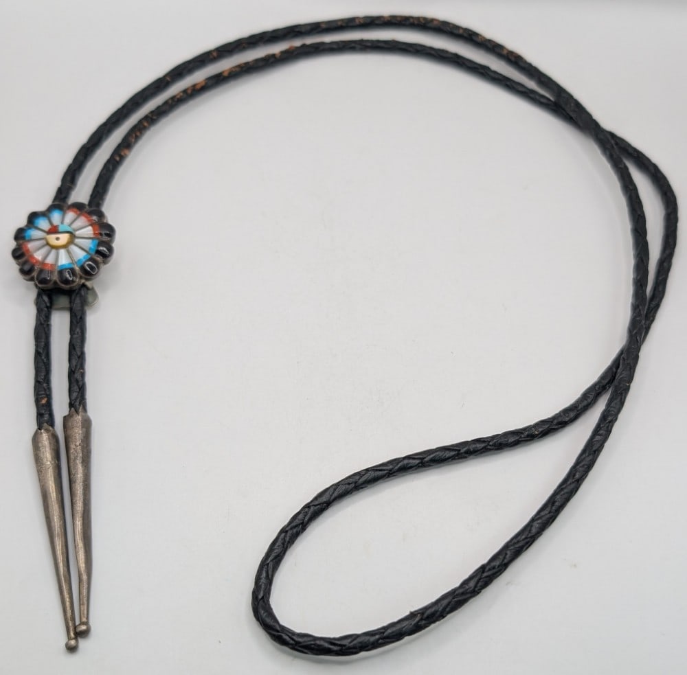 Sterling Native American Zuni Sunface Bolo Tie: Sterling Native American Zuni Sunface Bolo Tie. The bolo tie has Zuni's tribe symbol, the Sunface, made of onyx, turquoise, coral, and mother-of-pearl. It measures 20-1/4" length and the symbol measur