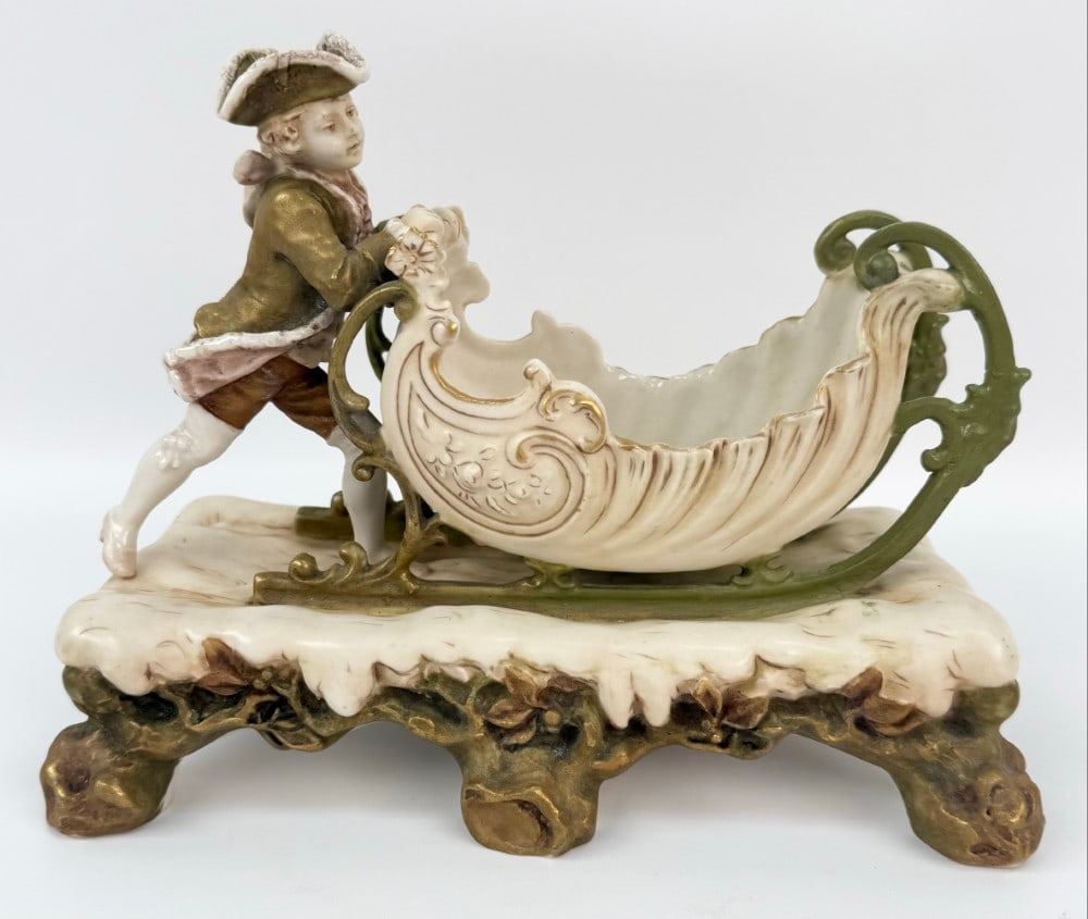 Antique Royal Dux Bohemia Boy Pushing Sleigh Vase Cache: Antique Royal Dux Bohemia Boy Pushing Sleigh Vase Cache. The vase is marked on the base and is number 844. The condition is nice with gold accents. Measures approximately 7-3/4" tall x 10" across x 5"
