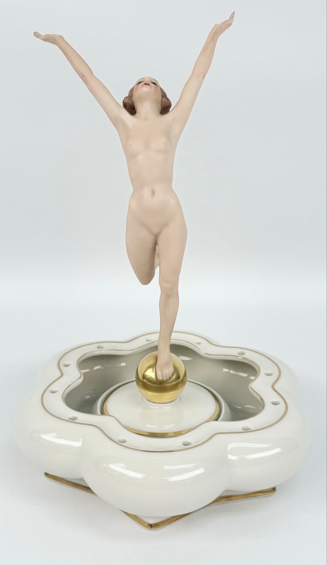 Hutschenreuther "Sun Child" Art Deco Porcelain Figurine On Flower Frog Base: Hutschenreuther "Sun Child" Art Deco Porcelain Figurine On Flower Frog Base. The figurine features a nude woman with outstretched arms standing on a gold painted ball. The Art Deco set was designed by