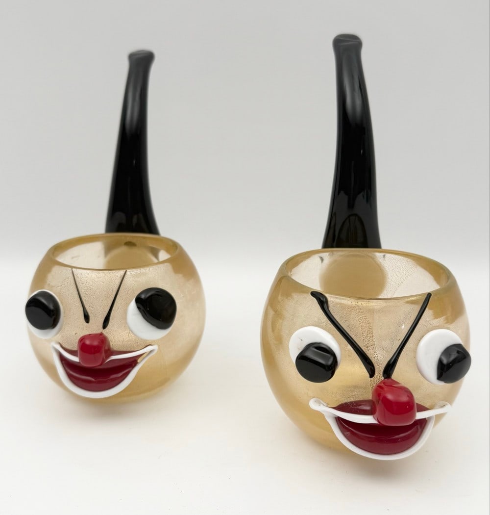 Pair Of Vintage Murano Glass Clown Pipes: Pair of vintage Murano glass clown pipes with applied faces. The bowls features gold fleck and the stem is black glass, face components are applied. They are in excellent condition with no chips or cr